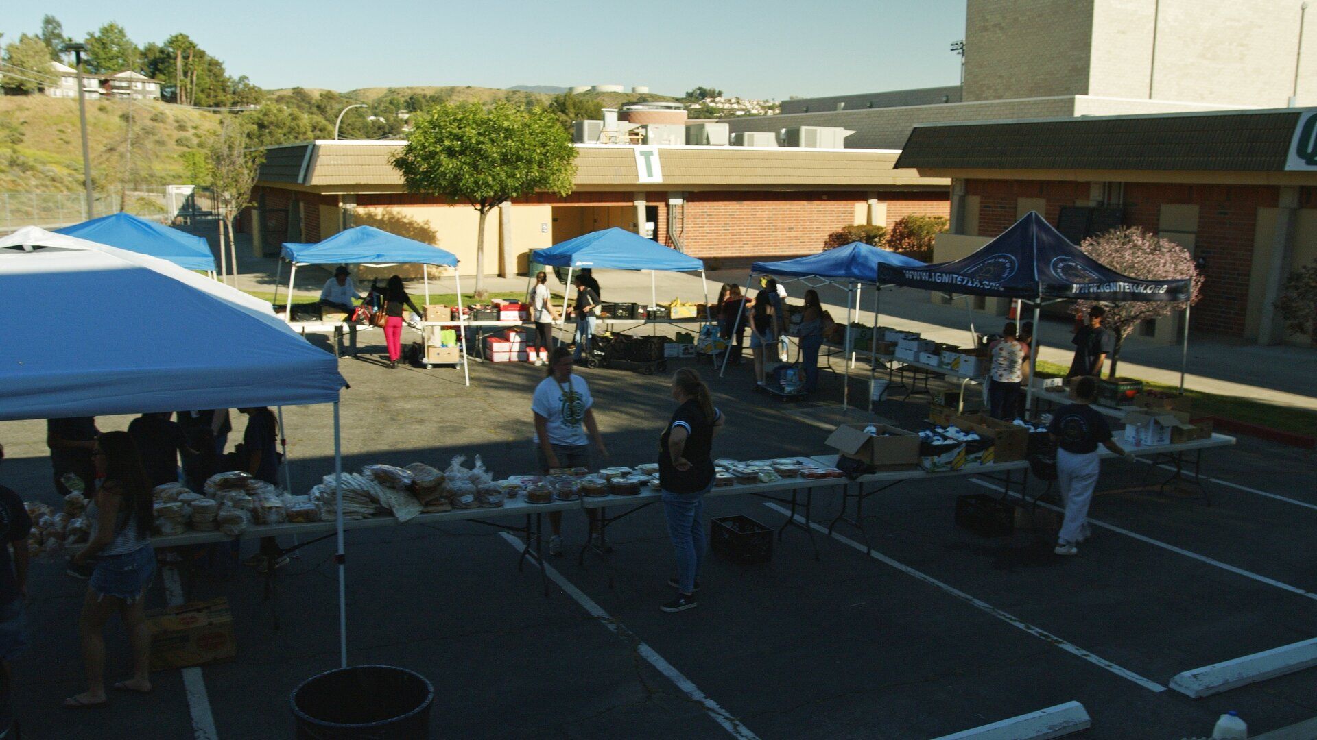 Volunteers set out tables of free groceries under blue tents at a Friday distribution
