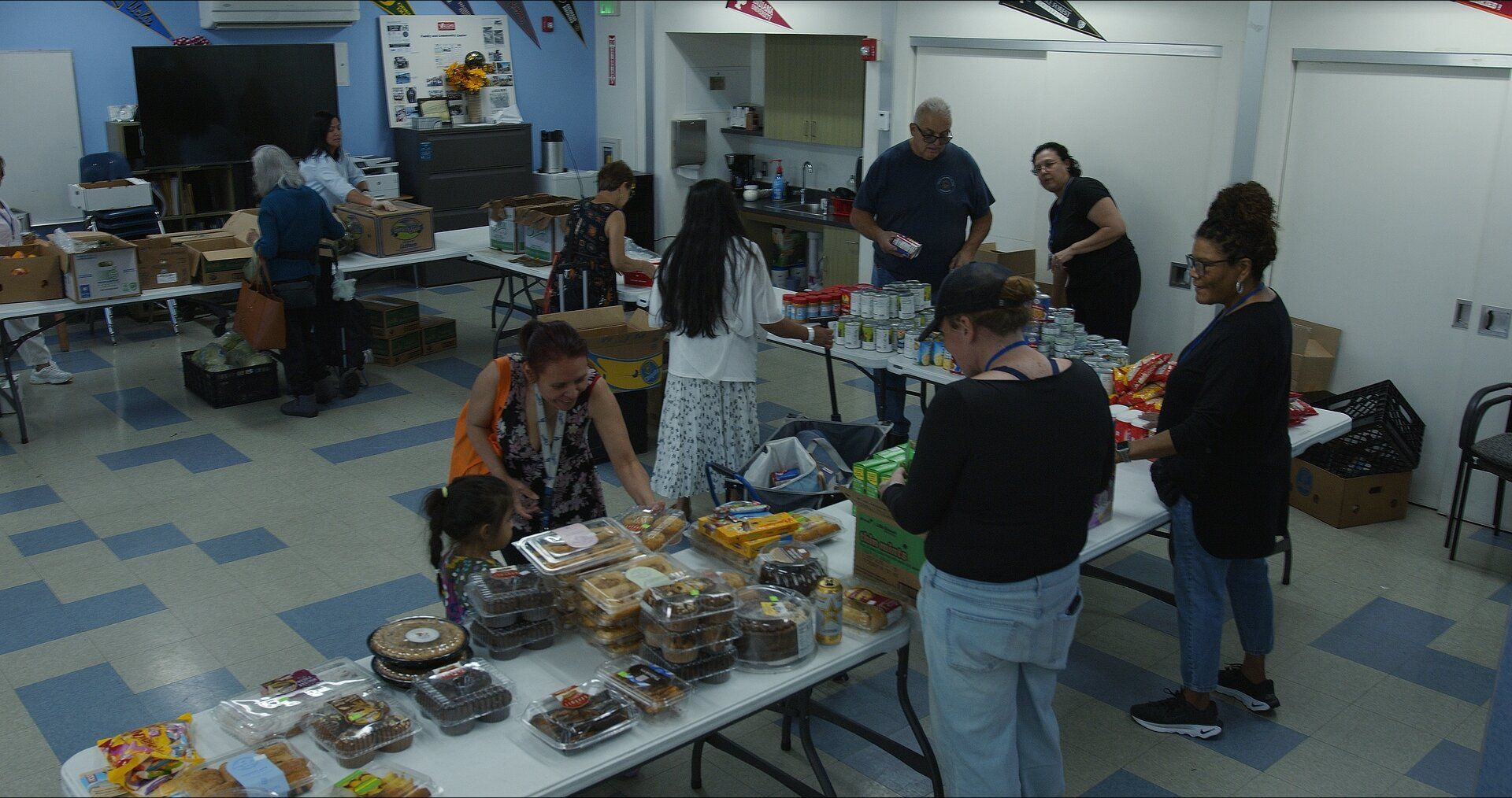 Volunteers set out groceries and baked goods on tables at an indoor distribution